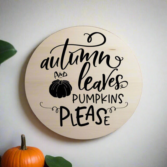 Round wooden sign with black text 'autumn and leaves pumpkins please' on a white background
